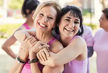 women smiling and hugging at breast cancer awareness event