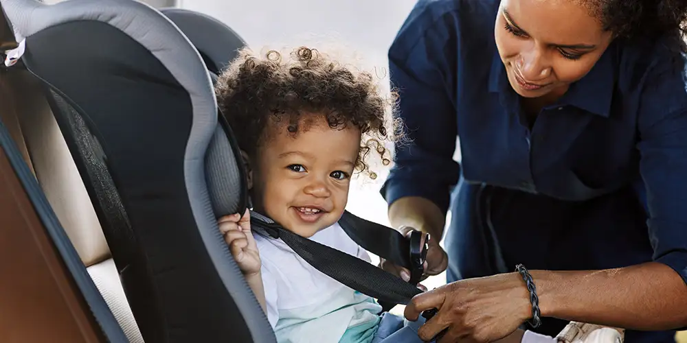 mom buckling toddler into car seat
