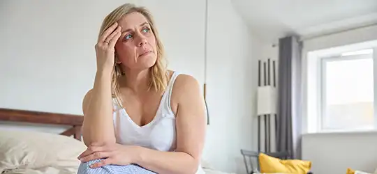 woman sitting on bed holding her head