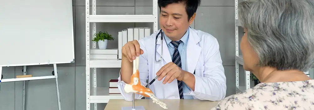 doctor pointing to a model of a foot while speaking to a patient