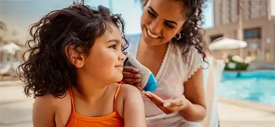 mom putting sunscreen on her daughter at the pool