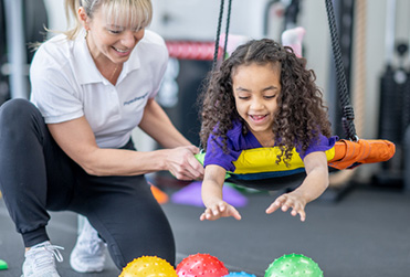 Young girl swinging for sensory balls at the Knights of Columbus Developmental Center