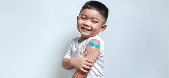 young boy showing arm with two band-aids post vaccinations